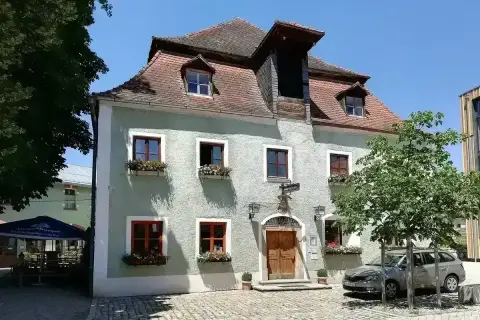 Pale green rendered inn with a steep tiled roof, dormers, red-framed windows and flower boxes