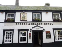 White and black painted inn front with a lettered fascia, sash windows and window boxes