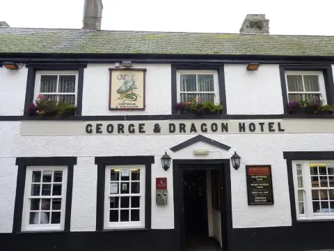White and black painted inn front with a lettered fascia, sash windows and window boxes