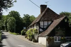 Long tile-hung and timber-framed inn on a bend in the village street, hanging baskets along its front