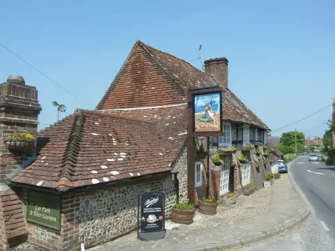 Flint and timber inn on a corner, swept tiled roof and a painted sign of St George on a tall post