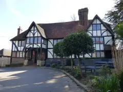Large half-timbered inn with a tiled roof and clipped bay trees, benches on the forecourt