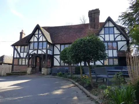 Large half-timbered inn with a tiled roof and clipped bay trees, benches on the forecourt