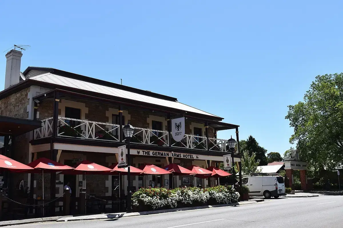 Two-storey stone hotel with a timber verandah, painted sign and red parasols along the footpath