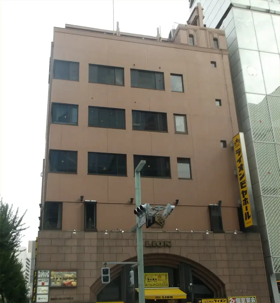 Brick-faced building with a carved lion over an arched entrance and a yellow Lion beer hall banner