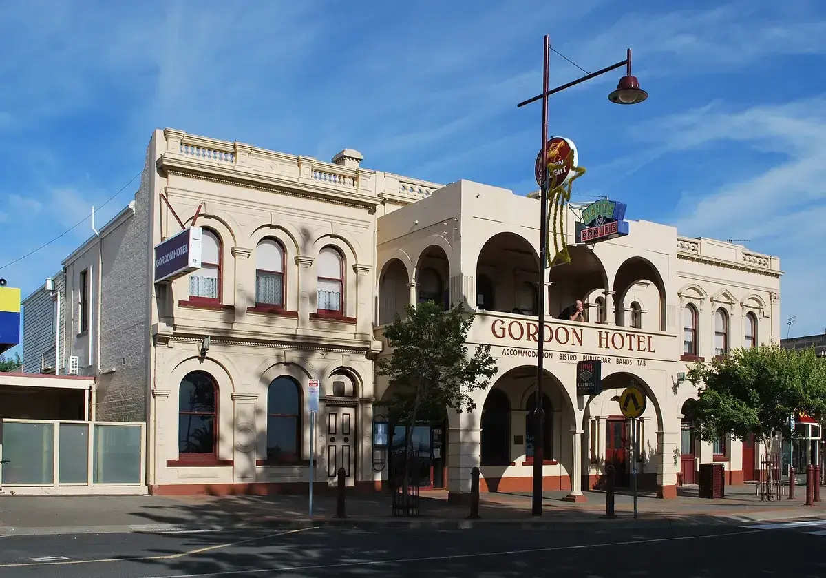 Cream rendered hotel with an arcaded upper balcony and rounded arches, on a wide street corner