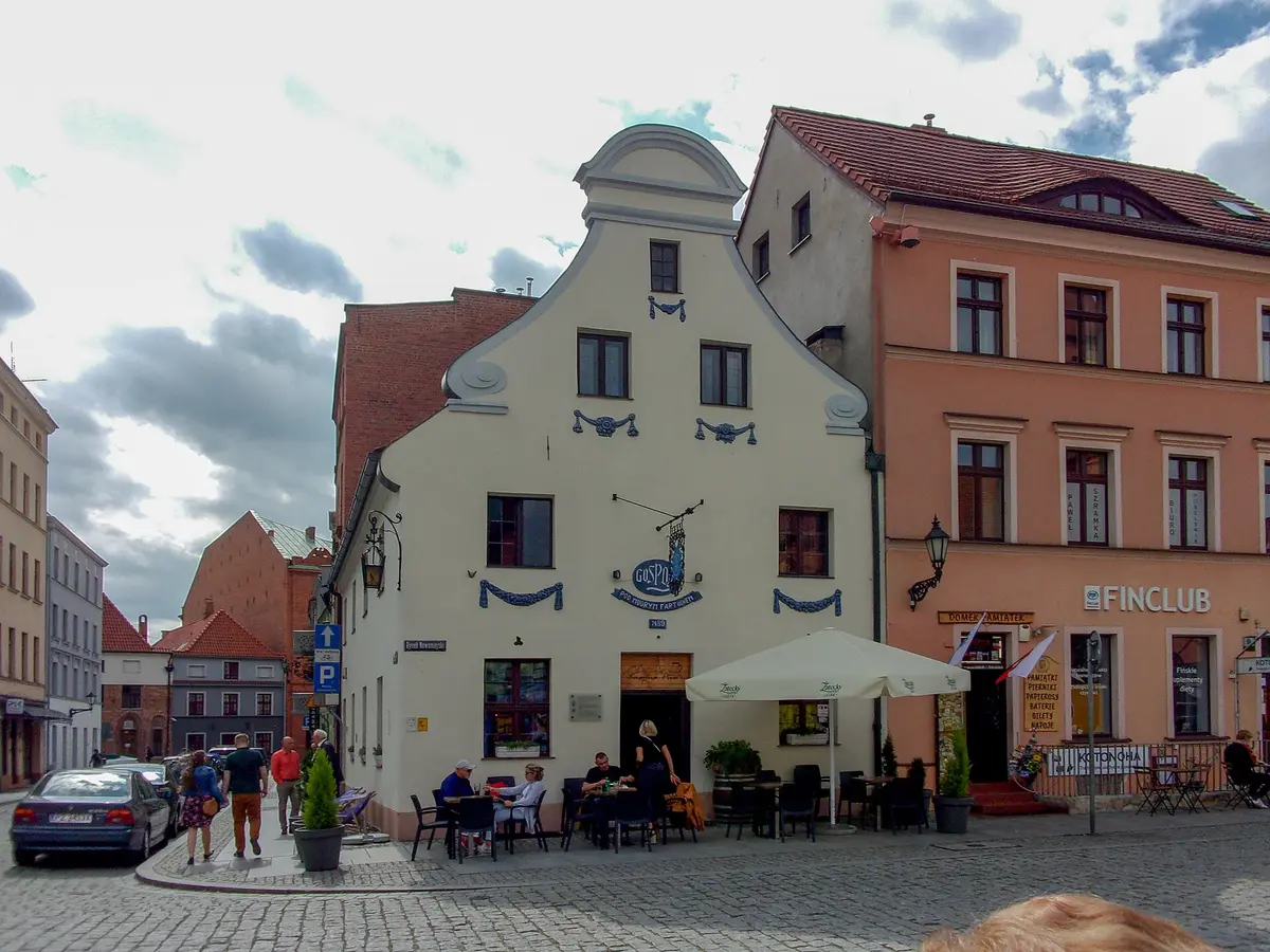 Cream gabled house on a cobbled square, a blue Gospoda Pod Modrym Fartuchem sign hung from its front