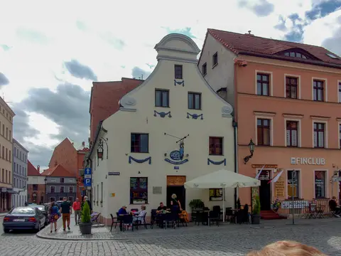 Cream gabled house on a cobbled square, a blue Gospoda Pod Modrym Fartuchem sign hung from its front