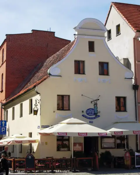 The scrolled gable in sunlight, the wrought-iron inn sign and the date 1489 painted beneath it