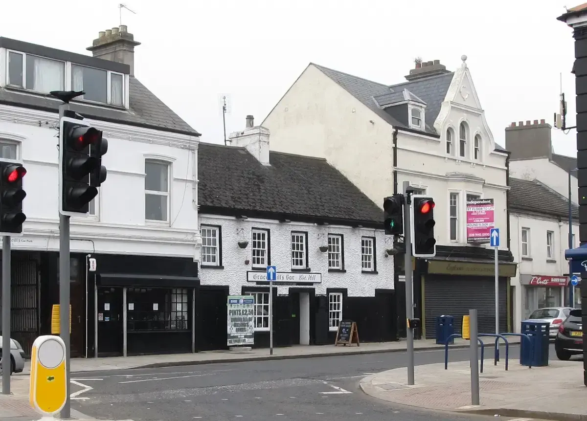 Low whitewashed pub with black window frames and a slate roof, set back on a town high street