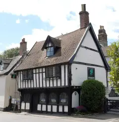 Jettied timber-framed inn with a dormer and a green dragon sign, brick stacks above