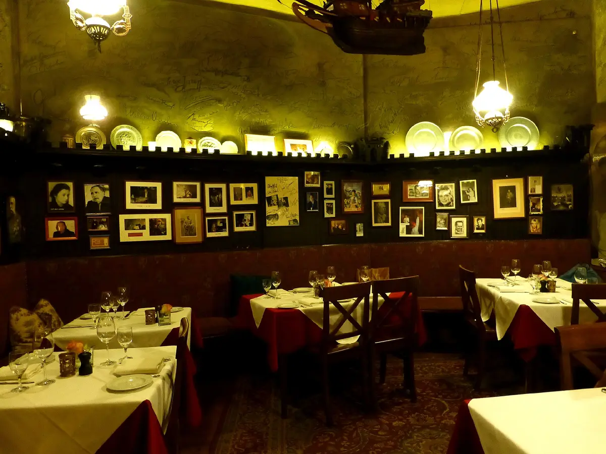 A low vaulted dining room hung with framed photographs, tables laid with white cloths under oil lamps