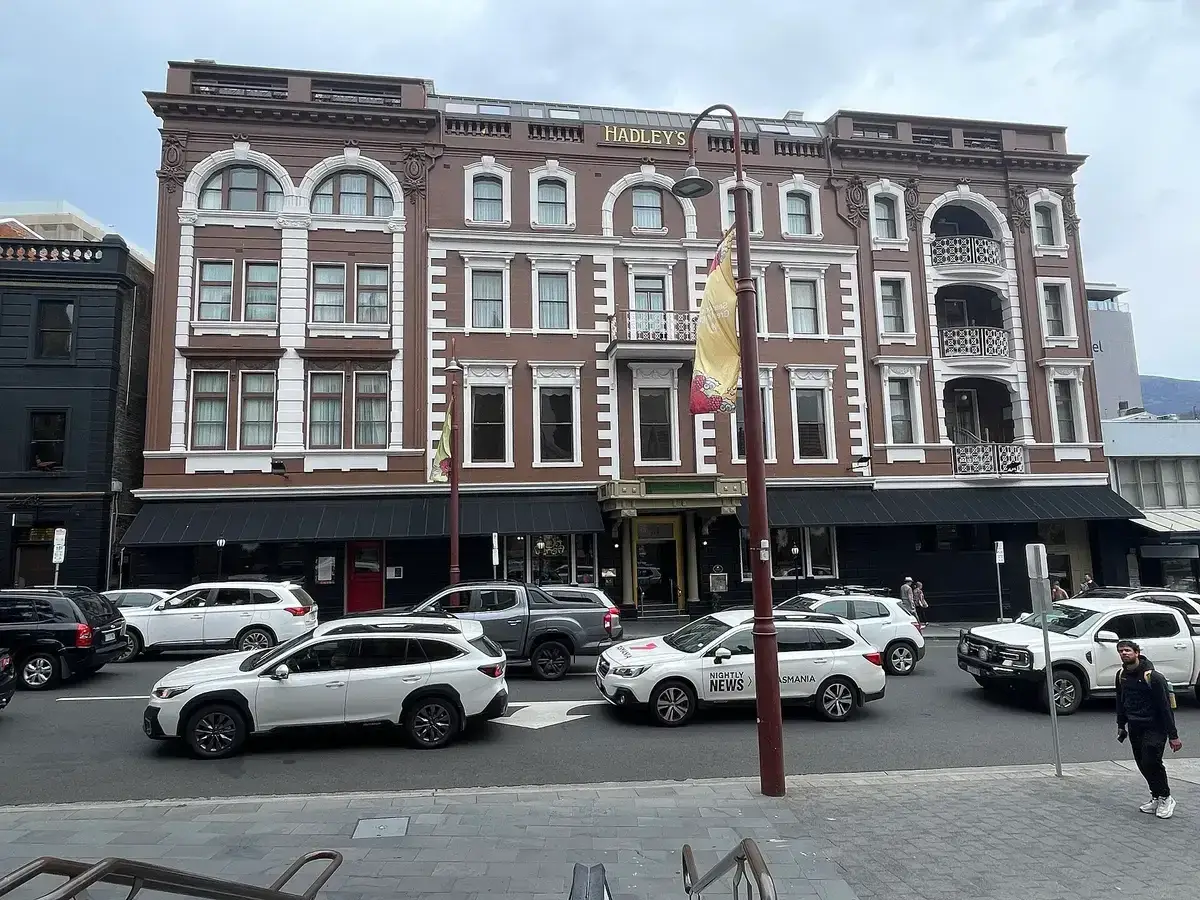 Four-storey brown and white hotel front lettered Hadley's, awnings over the footpath, cars outside