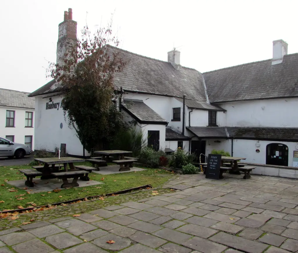 Whitewashed pub with slate roofs around a flagged yard of picnic tables, its name on the gable