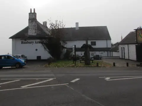 The whitewashed pub across a road in fog, name painted on the gable and a carved post in the garden