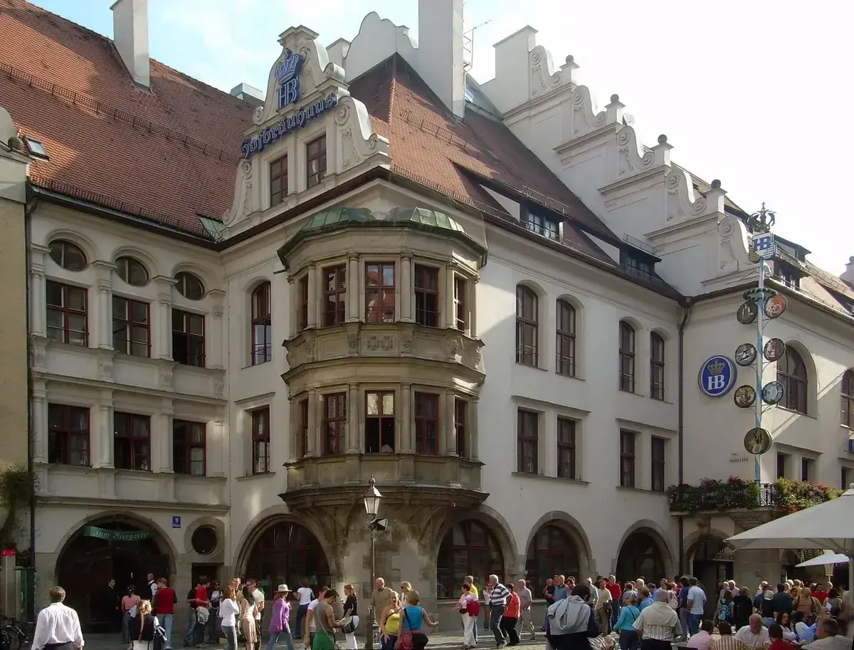 White gabled beer hall with an arcaded ground floor, oriel window and blue Hofbrauhaus lettering