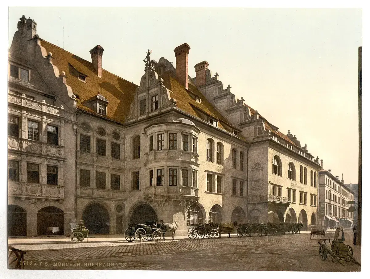 Horse-drawn cabs waiting under the arcades of the Hofbrauhaus, with its oriel window and stepped gables