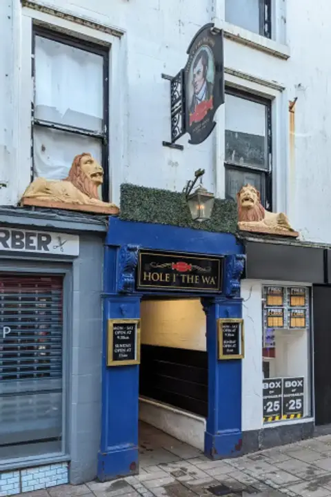 The entrance to the Hole i' the Wa' painted blue, with a Robert Burns inn sign and two stone lions above