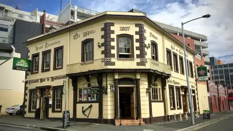 Cream corner tavern with brown quoins, an iron balcony and painted lettering including 1807