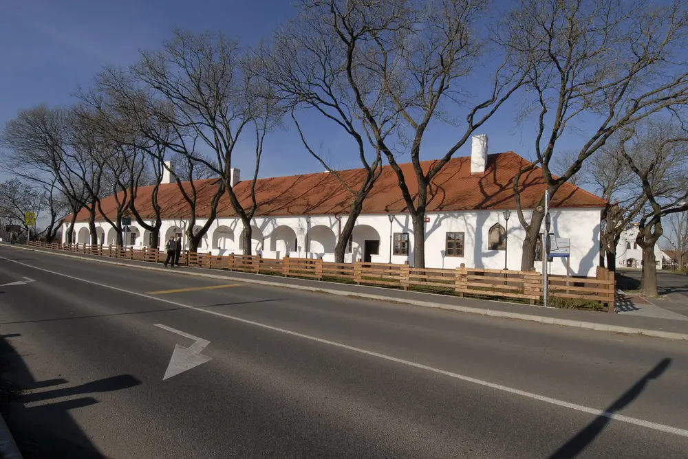Long whitewashed inn with an arcade of seven arches and a red tiled roof, bare trees along the road