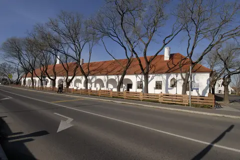 Long whitewashed inn with an arcade of seven arches and a red tiled roof, bare trees along the road