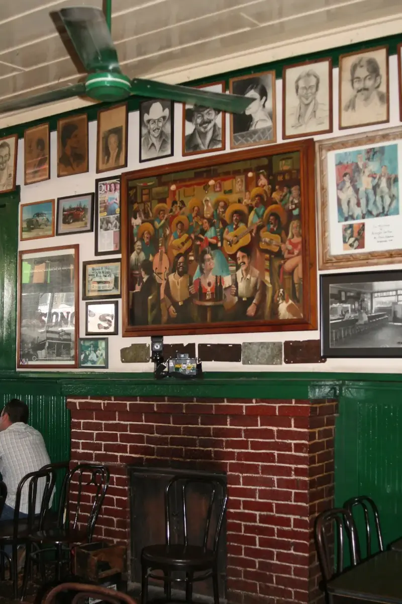 Green panelled cantina wall hung with pencil portraits above a brick chimney breast and bentwood chairs