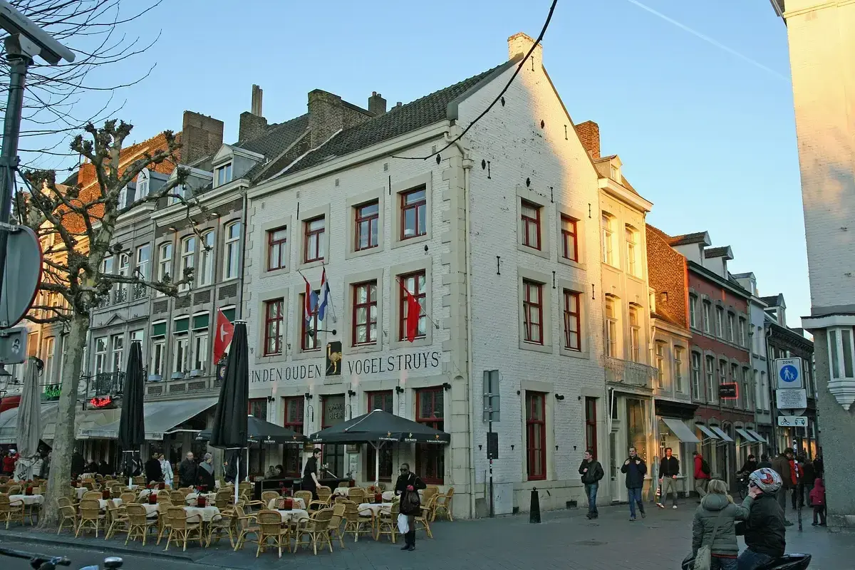 White gabled corner house on the Vrijthof lettered In den Ouden Vogelstruys, café tables in front