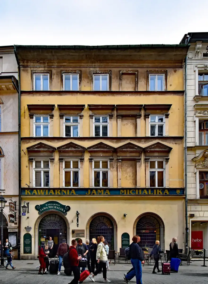 Four-storey ochre tenement with three arched windows and a painted Kawiarnia Jama Michalika fascia