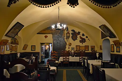 Vaulted café room hung with framed drawings, dark panelled benches, laid tables and a small chandelier