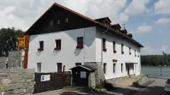 White rendered inn with a dark timber gable and dormers, above a granite wall by a reservoir