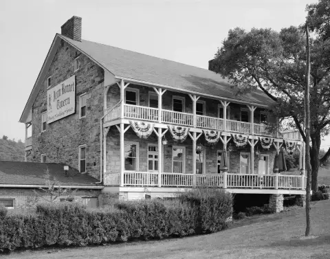 Two-storey fieldstone tavern with a white timber verandah on two levels and a painted sign