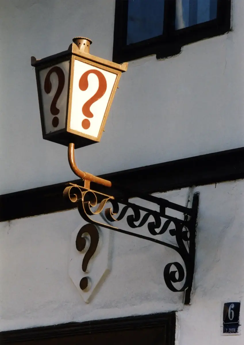A gilded lantern bracket carrying a single red question mark, with a second question mark on the sign below it