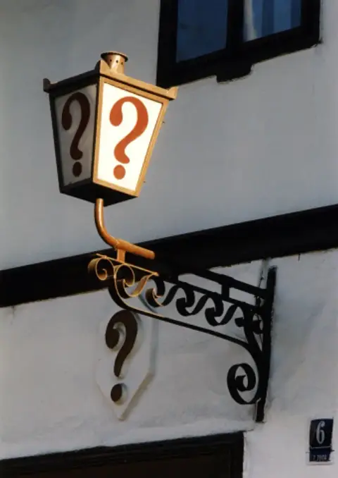 A gilded lantern bracket carrying a single red question mark, with a second question mark on the sign below it