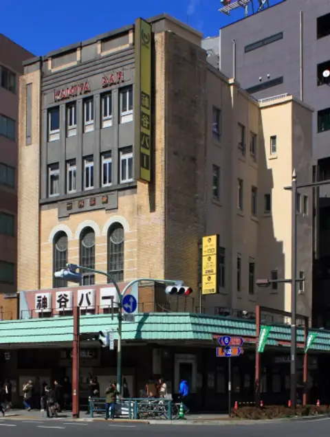 Four-storey buff-brick bar building with red roof lettering and a tall vertical sign in Japanese