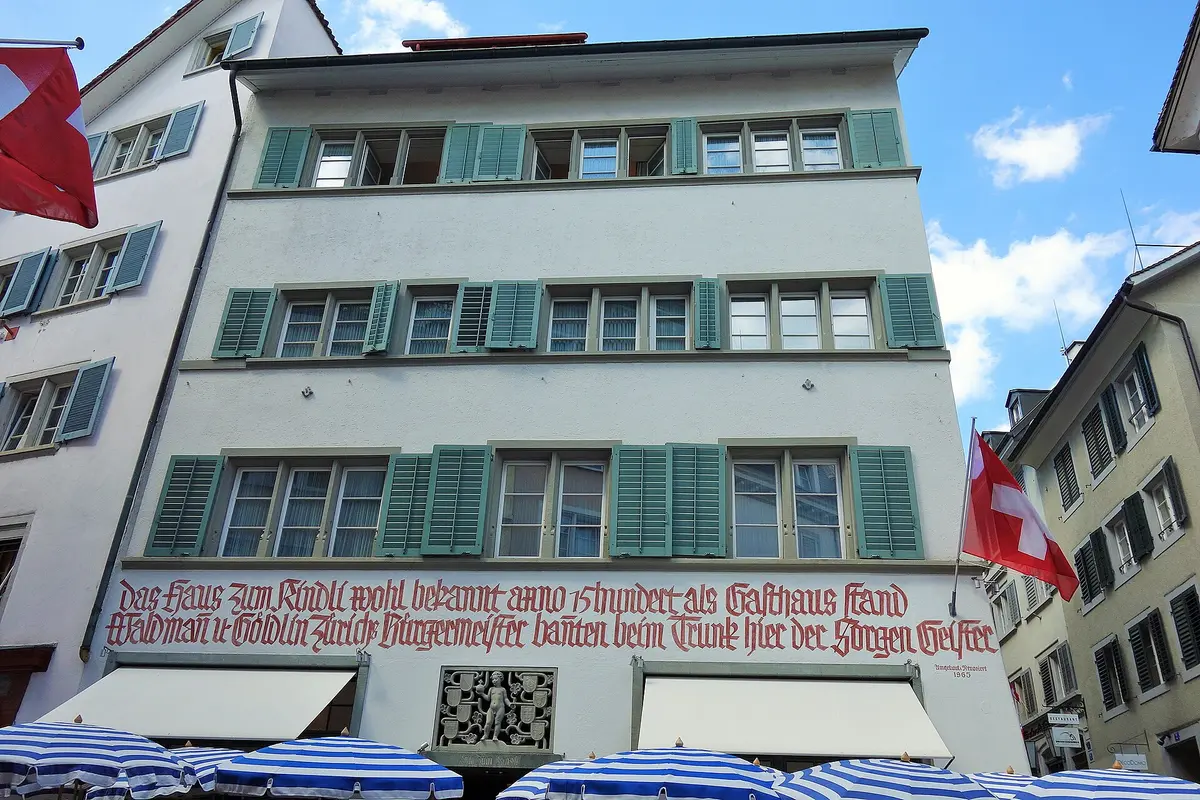 White house front with red Gothic lettering across it and a carved child panel between two awnings