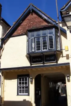 Cream-rendered inn with a leaded oriel window lettered Kings Head above a stone archway