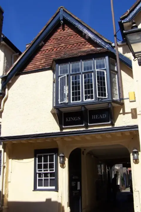 Cream-rendered inn with a leaded oriel window lettered Kings Head above a stone archway
