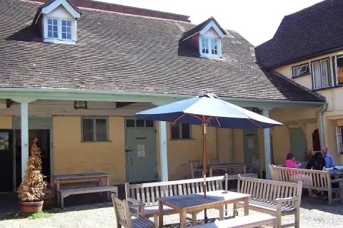 Cobbled yard with a colonnade of wooden posts, dormer windows above and tables under a parasol