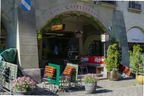 Cellar tavern entrance under a Bern arcade, hanging Klötzlikeller sign and a red bar counter by the steps
