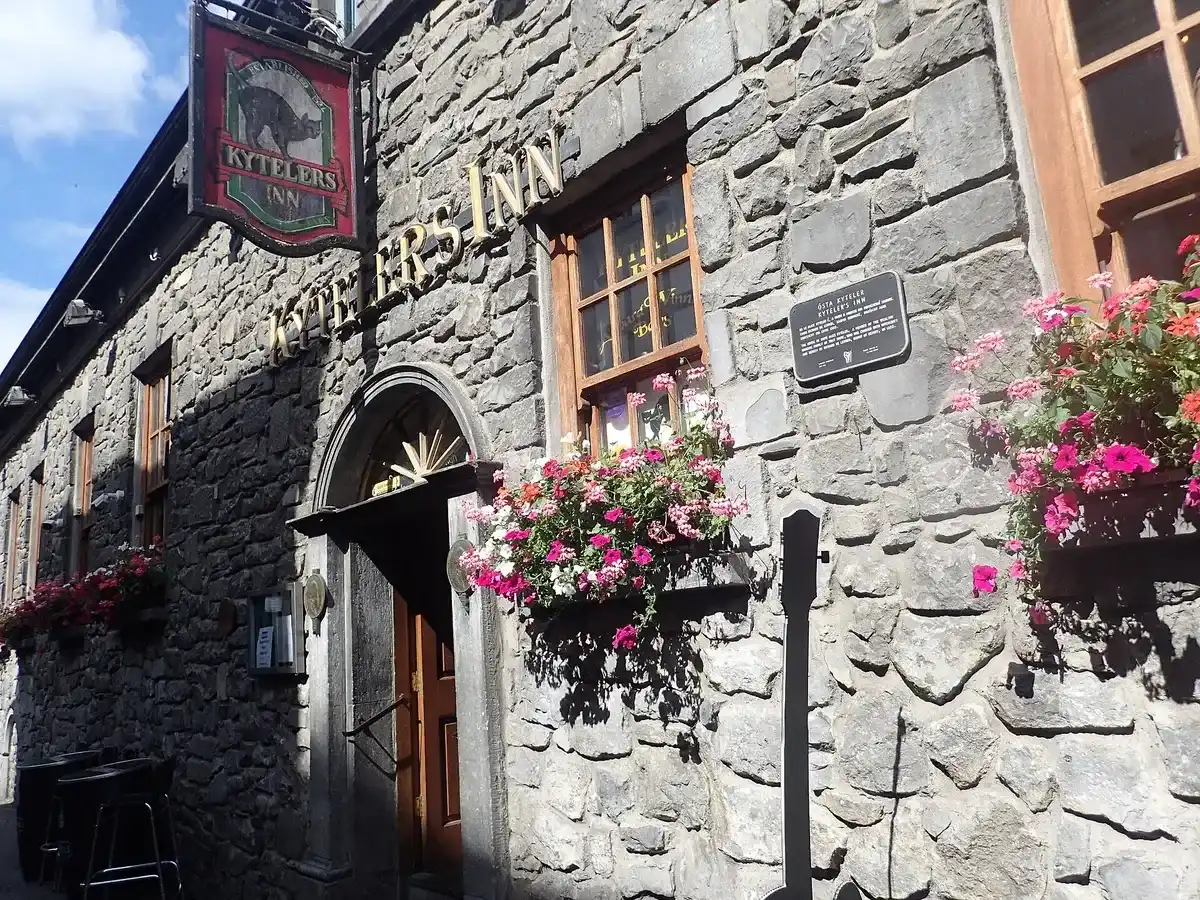 Stone front of Kyteler’s Inn in sunlight, gilt lettering over the arched door and a painted hanging sign