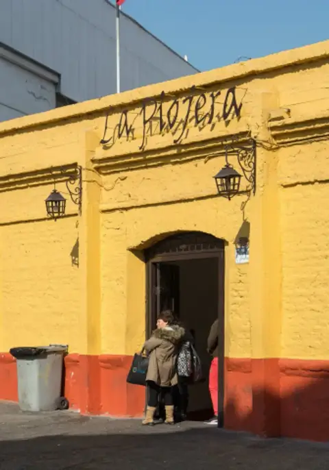 Yellow-painted adobe wall with the bar's name in black script above an open doorway and lanterns