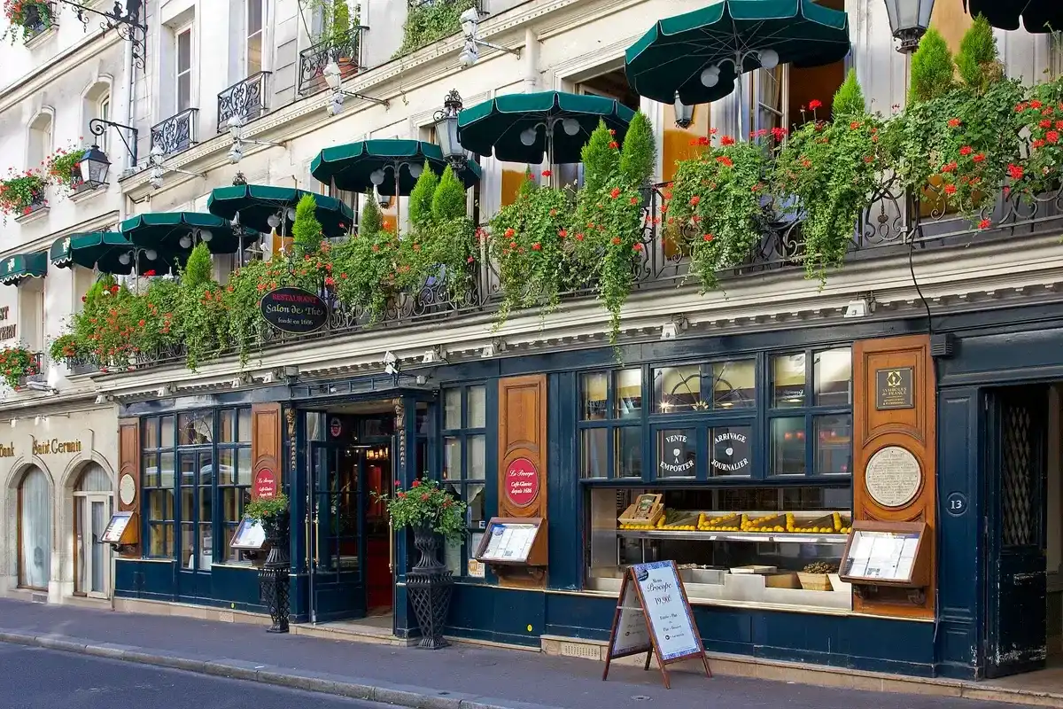 Dark blue front with lanterns, window boxes of geraniums and green parasols above, on a quiet street