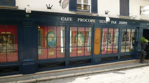 Cream shopfront lettered Café Procope tenu par Zoppi, with framed portraits in its windows