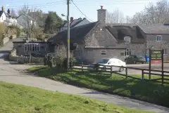 Thatched stone inn with its name in gold on the gable, beside a lane climbing out of the village