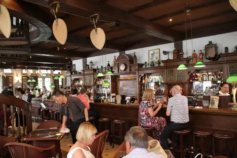 The bar from the other end, wooden punkah fans above and drinkers along the counter