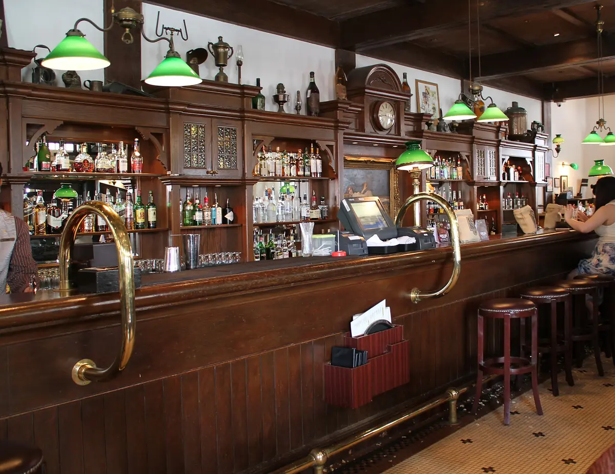 Long timber bar counter with green glass lampshades, brass rails and peanut shells on the floor