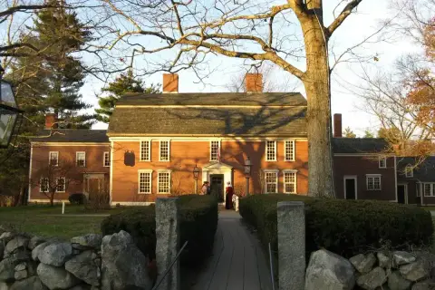 Red clapboard inn with brick chimneys and white sash windows, behind a stone wall and hedge