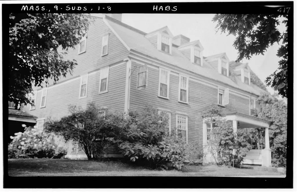 The clapboarded Wayside Inn with its dormers and porch, behind shrubs, photographed for a survey about 1935