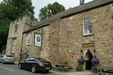 Long stone inn with a battlemented tower at one end, arched windows and a painted hanging sign