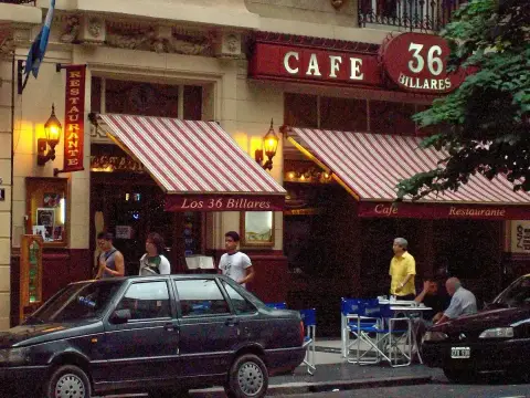 The same front at dusk, striped awnings out and people at the pavement tables